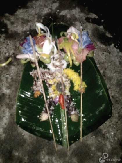 Multicolored figure offered with incense, holy water, flowers and rice. (Photo by Garrett Kam)